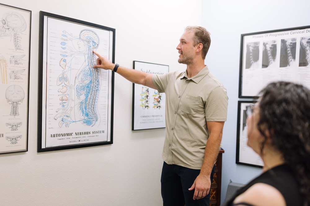 Chiropractor explaining the autonomic nervous system to a patient using a wall chart in Mission Valley, San Diego, CA