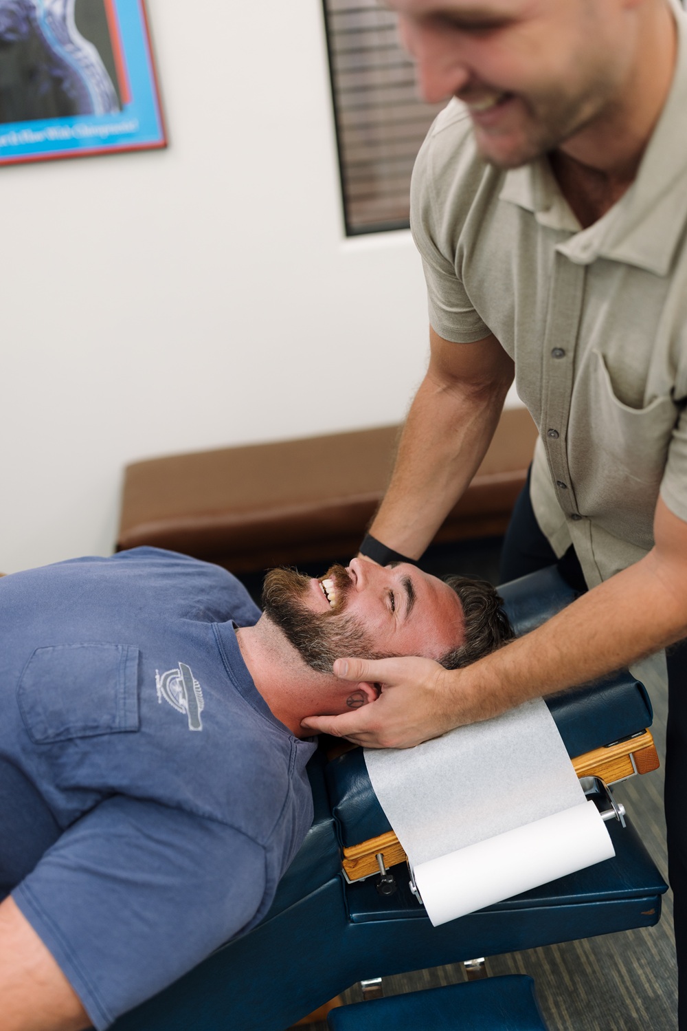 Chiropractor performing a neck adjustment on a smiling patient lying on a treatment table 