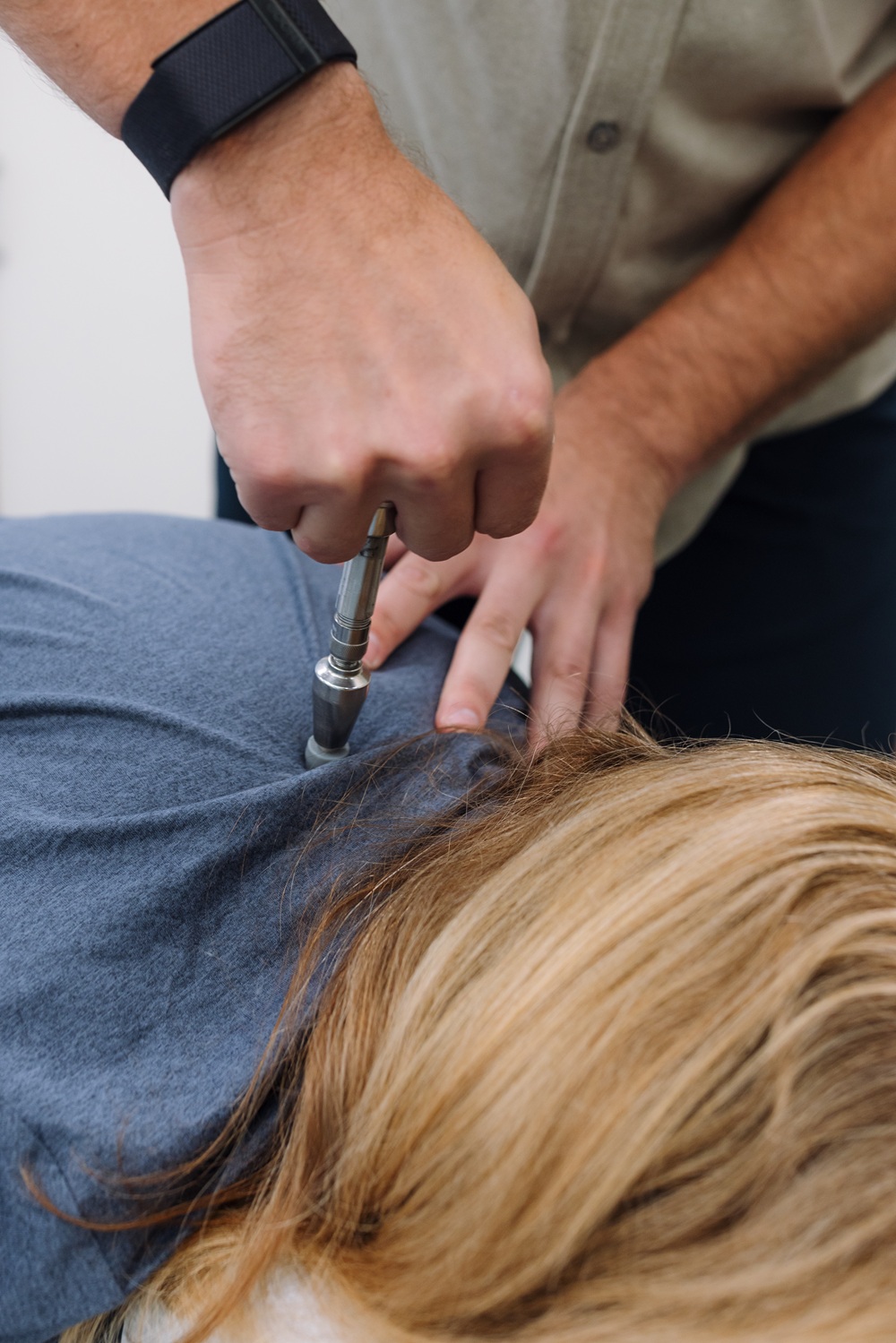 Chiropractor using a handheld adjusting instrument on a patient's upper back 